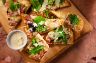 This unique appetizer pizza–and great party food idea–features thin crispy flatbread baked golden and delicious topped with crisp peppered bacon and gooey melted Italian cheese. It’s finished with a drizzle of indulgent garlic Parmesan cream sauce, fresh spring greens and shaved Parmesan cheese. 