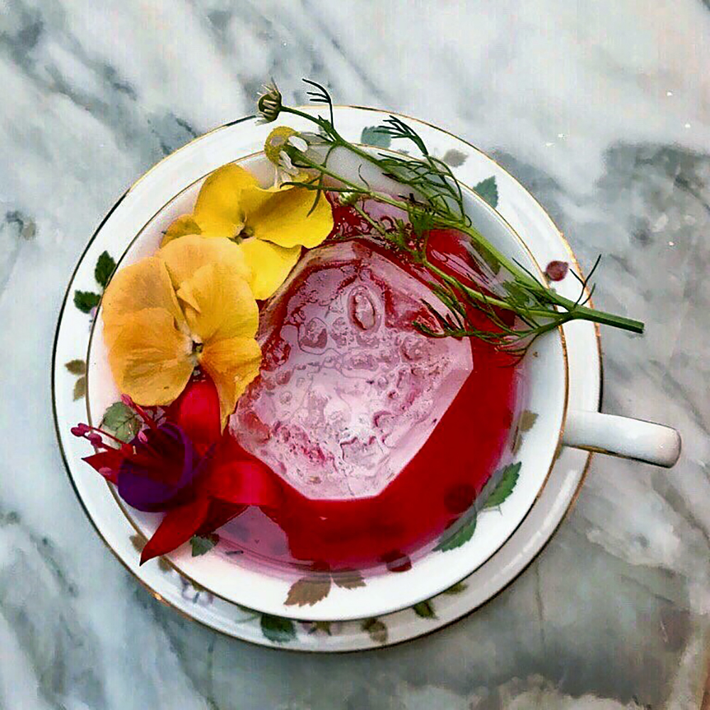 The Hibiscus & Rose Tea cocktail from the Deer Path Inn is served in a tea cup and made with Hibiscus rose cold tea, gin, Suze, tangerine juice, and Oleo Saccharum.