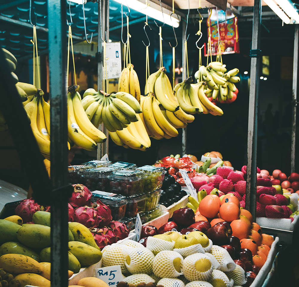 Bunches of fresh bananas hang in an open outdoor market. 