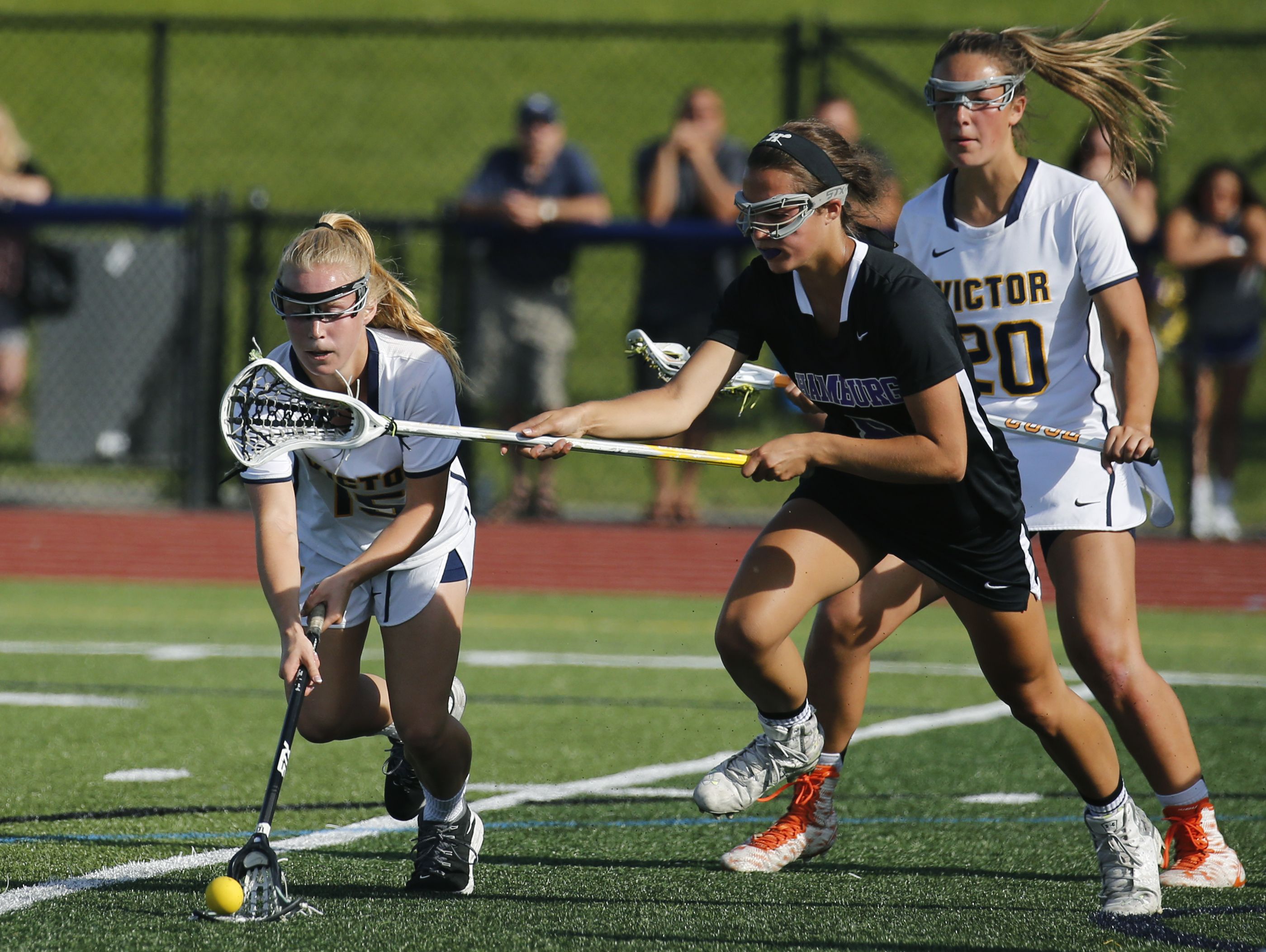 Victor's Kaci Messier picks up the ball under the stick of Hamburg's Bella Lettieri in the first half at Pittsford Sutherland High School.