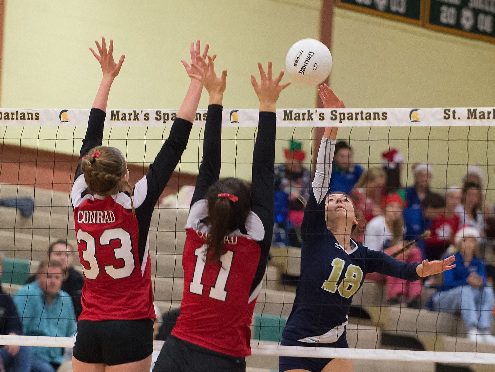 Delaware Military Academy's Nina Tindall (18) with a spike over the hands of Conrad's Julie Kulesza (33) and Madison Greer (11) in the second round game of the DIAA State Volleyball Tournament.