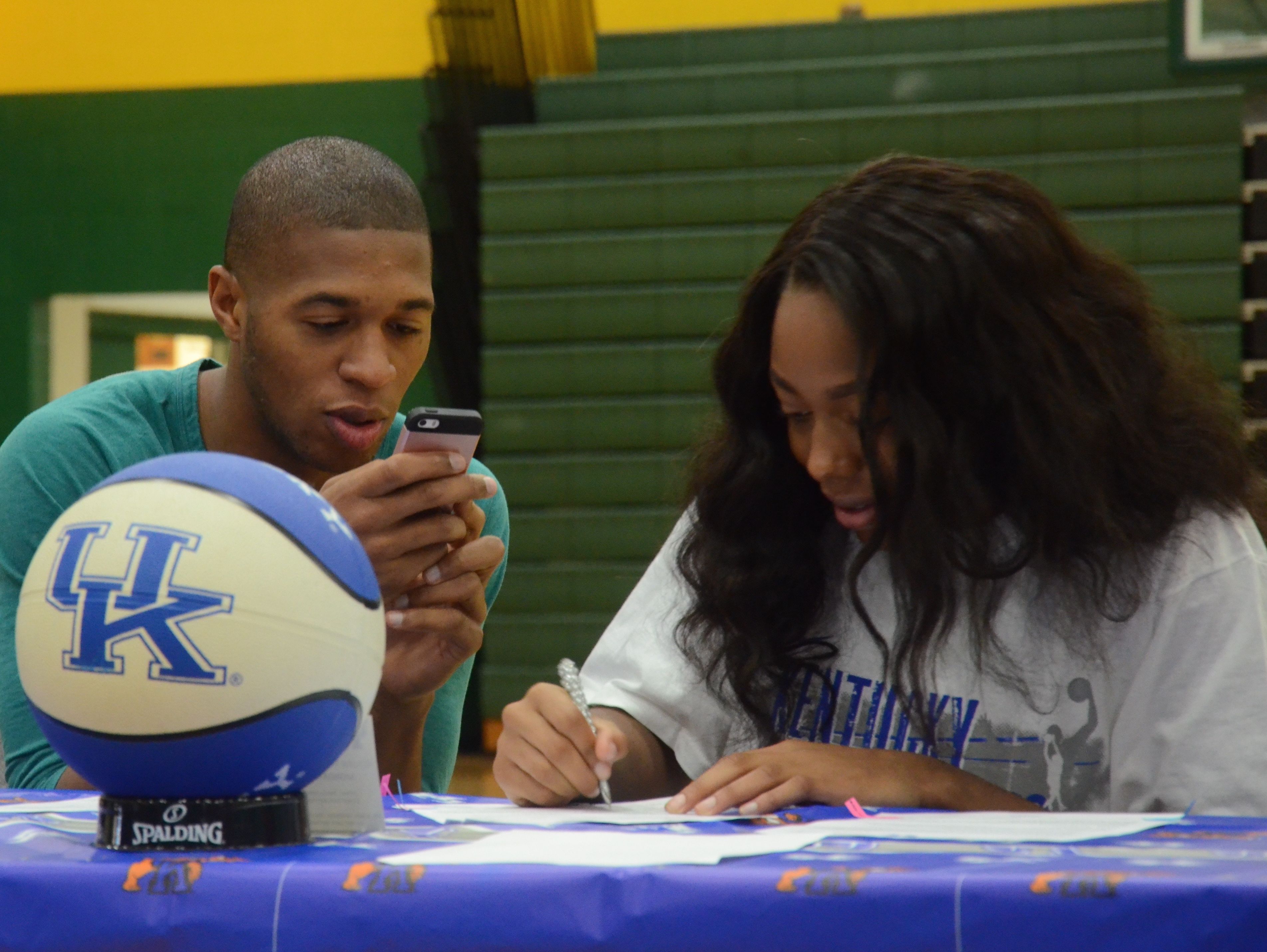Dorrie Harrison (right) signs a letter of intent to play basketball at Kentucky as her older bother Isaiah (left) captures the moment on camera.