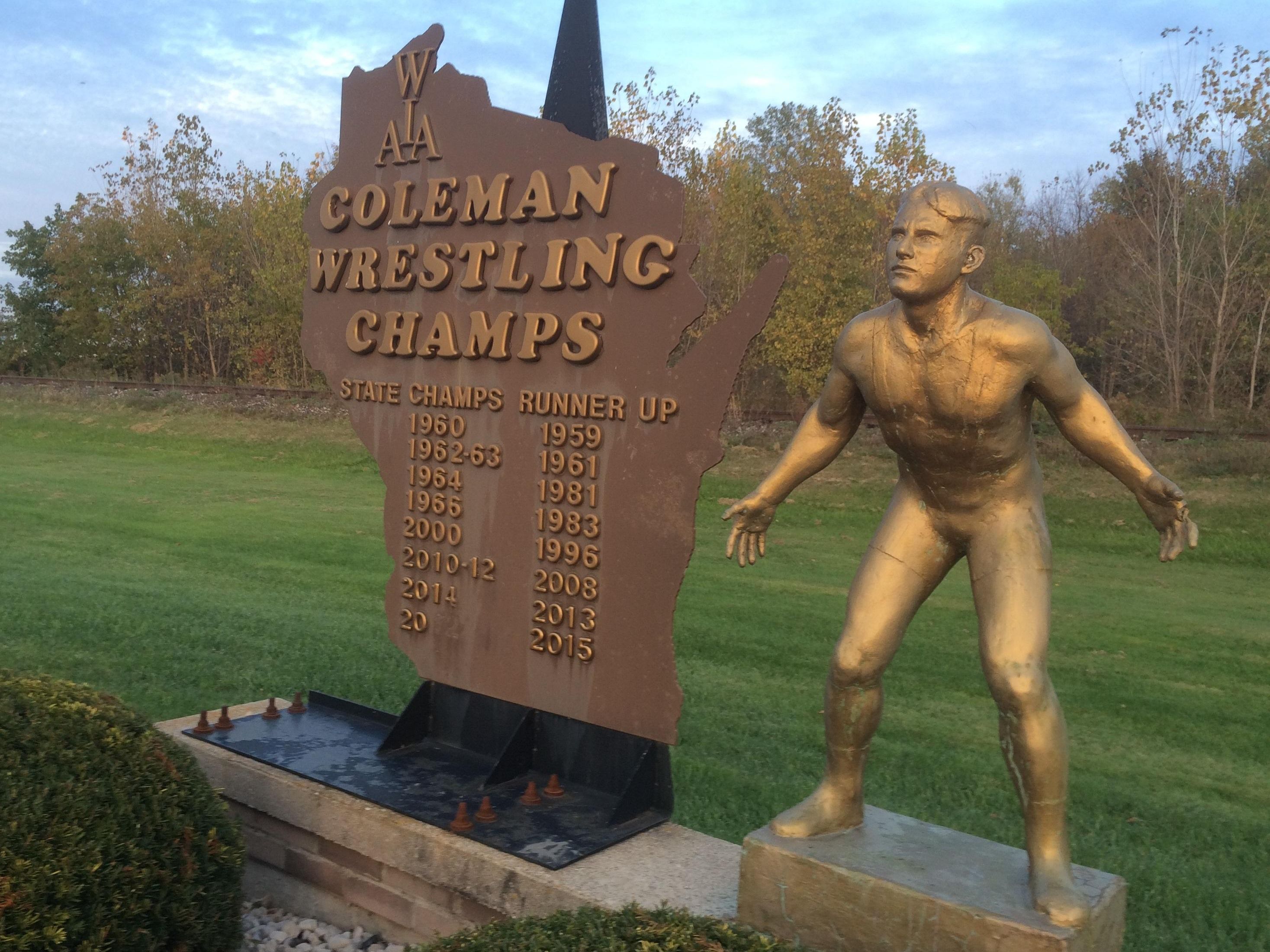A large-scale plaque and statue designed to resemble the appearance of the WIAA state championship trophy is positioned across the street from Coleman High School. The display features the years the school’s wrestling team has won its 13 state championships.